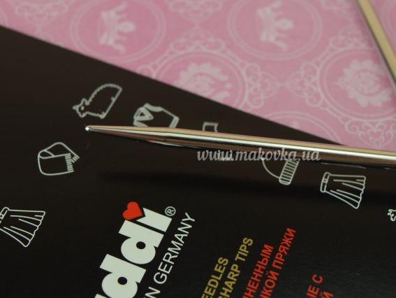 Макрофото подовженого кінчика металевої спиці ADDI Lace для точного та зручного в'язання. На задньому плані видно фірмову чорну упаковку з логотипом бренду та маркуванням серії.