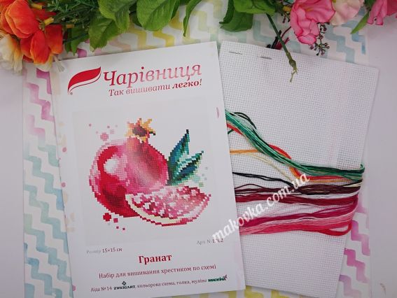 Обкладинка набору для вишивання «Гранат» від ТМ «Чарівниця» та яскраві нитки муліне червоних і зелених відтінків на декоративному фоні.
