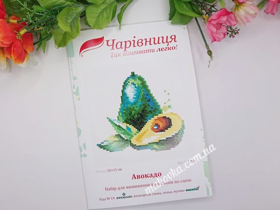 🎨 Детальний опис Набір для творчості в паперовій упаковці із зображенням вишитого авокадо. У верхній частині розміщено логотип «Чарівниця», знизу — назва «Авокадо» та перелік матеріалів. Фото доповнене декоративними зеленими листками та рожевими квітами по краях.