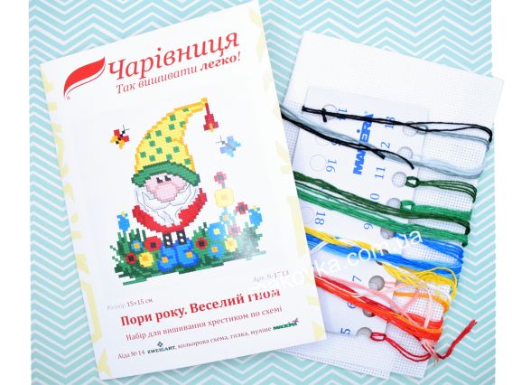 Обкладинка набору для вишивання N1713 Пори року. Веселий гном від ТМ «Чарівниця» поруч із білою канвою та пасмом ниток муліне червоних, жовтих, синіх та зелених кольорів.