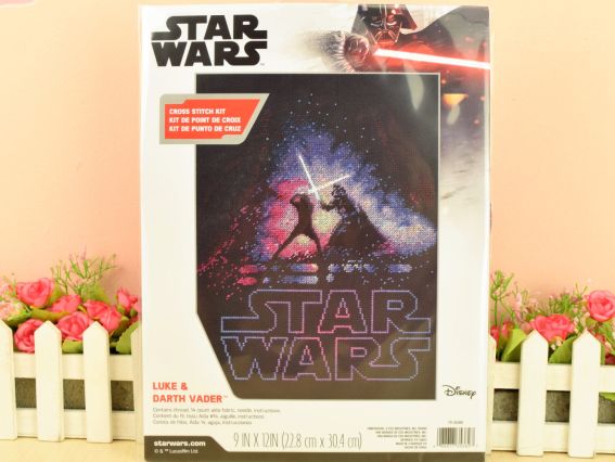 Фірмова картонна коробка набору для вишивання хрестиком Luke & Darth Vader від бренду Dimensions, що стоїть на світлому фоні з декоративними квітами та парканчиком.