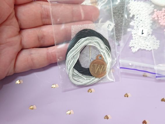 Нитки для зшивання деталей та металева фірмова лейбочка Wonderland Crafts у пакеті на долоні.